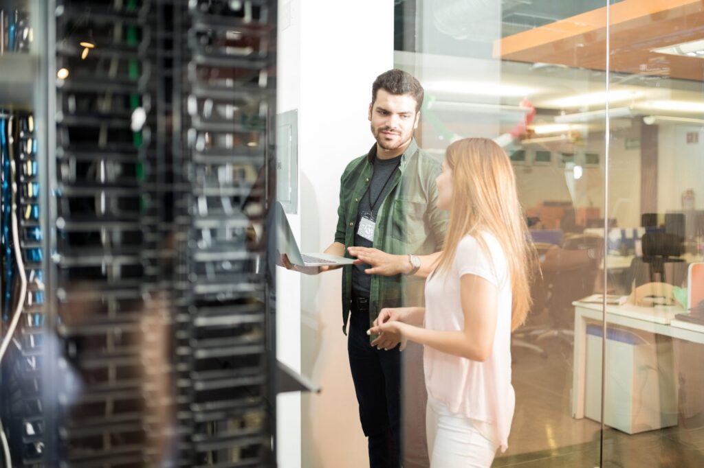 two-business-people-standing-server-room-with-laptop-discussing-1-scaled.jpg